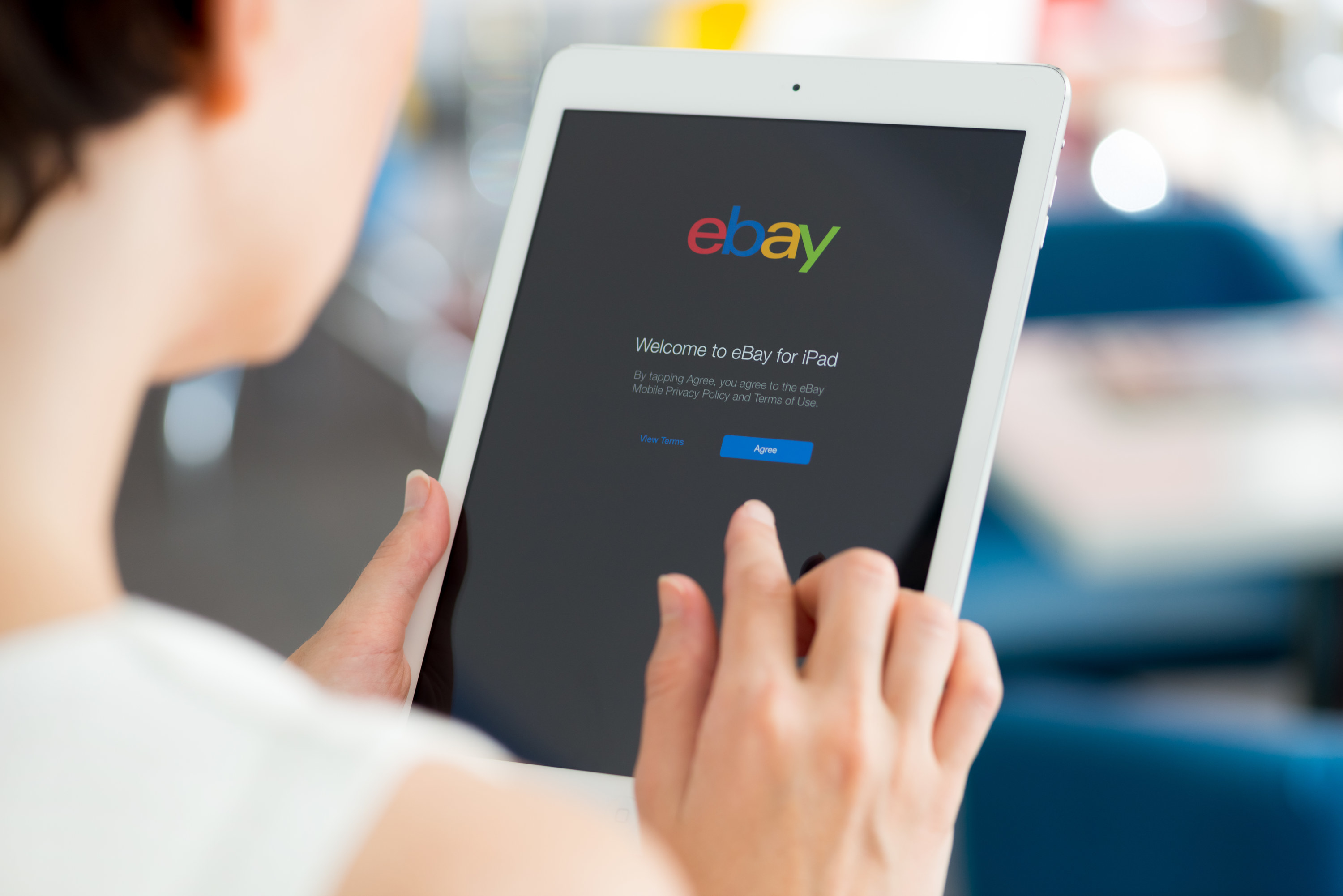 Woman holding a white Apple iPad Air with eBay welcome message on a screen