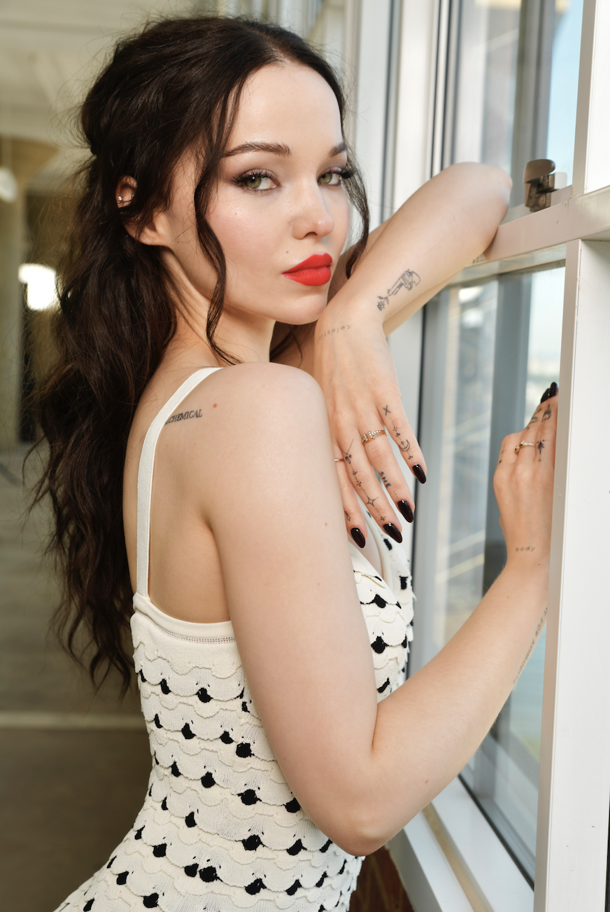 Close-up of Drew showing a tattoo on her arm as she leans against a window