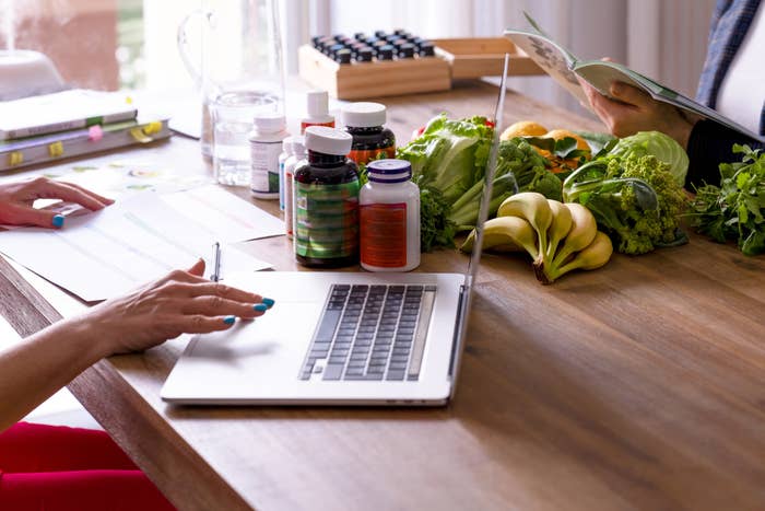 A nutritionist surrounded by vitamins and foods inputs stats into a laptop