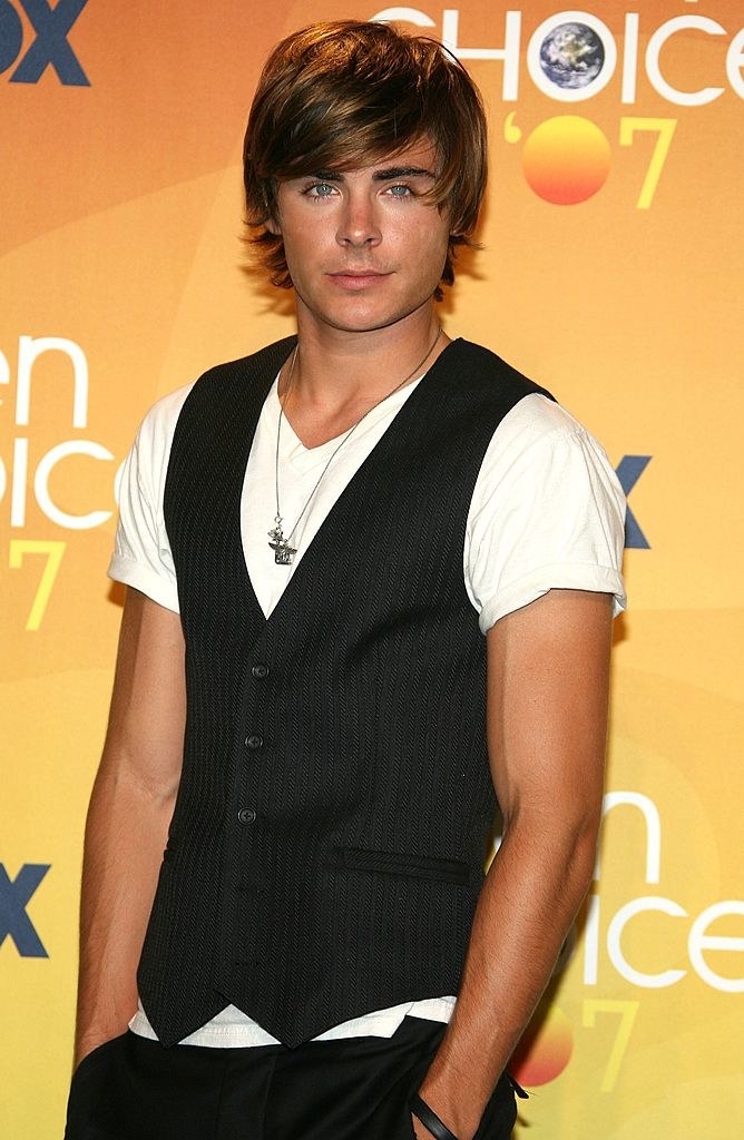 Closeup of Zac Efron wearing a vest over a plain T-shirt