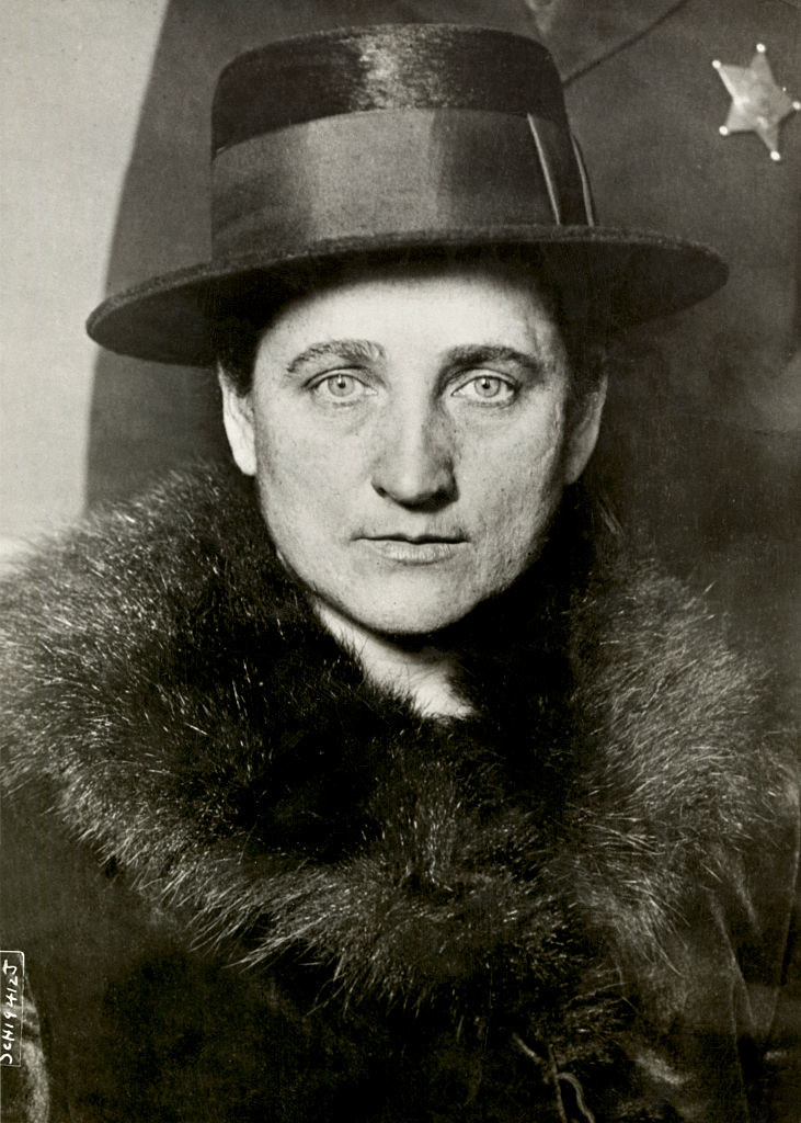 Tillie wearing a large hat and a fur trimmed coat