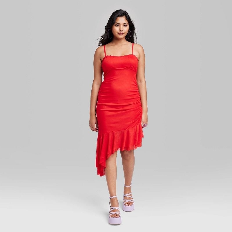 Model wearing red sleeveless midi dress with asymmetrical hemline, purple sandals