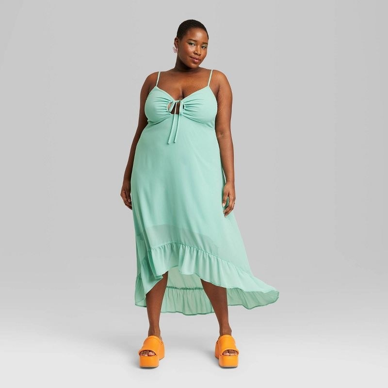 Model wearing high low chiffon dress in aqua green with orange shoes
