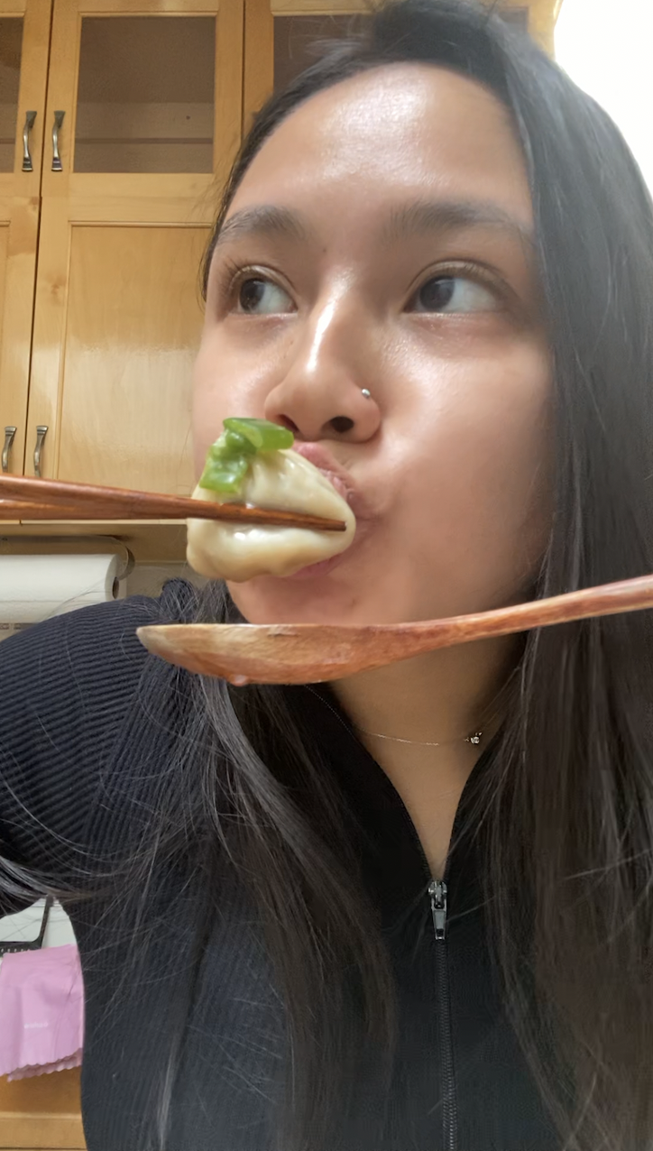 girl eating soup dumpling using chopsticks and spoon