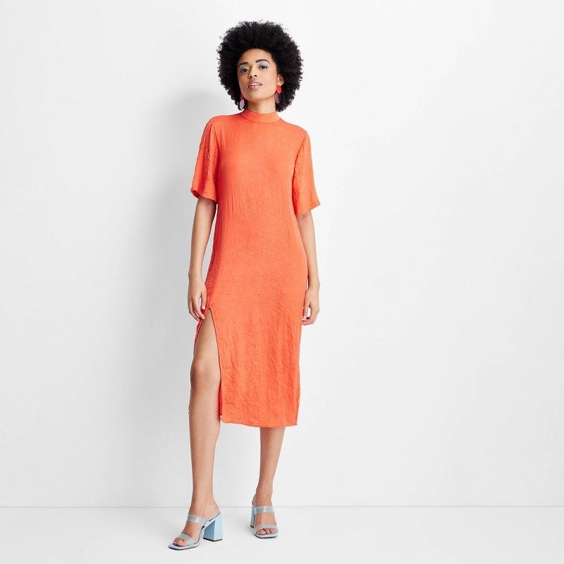 Model wearing mock neck orange midi dress with blue sandal heels