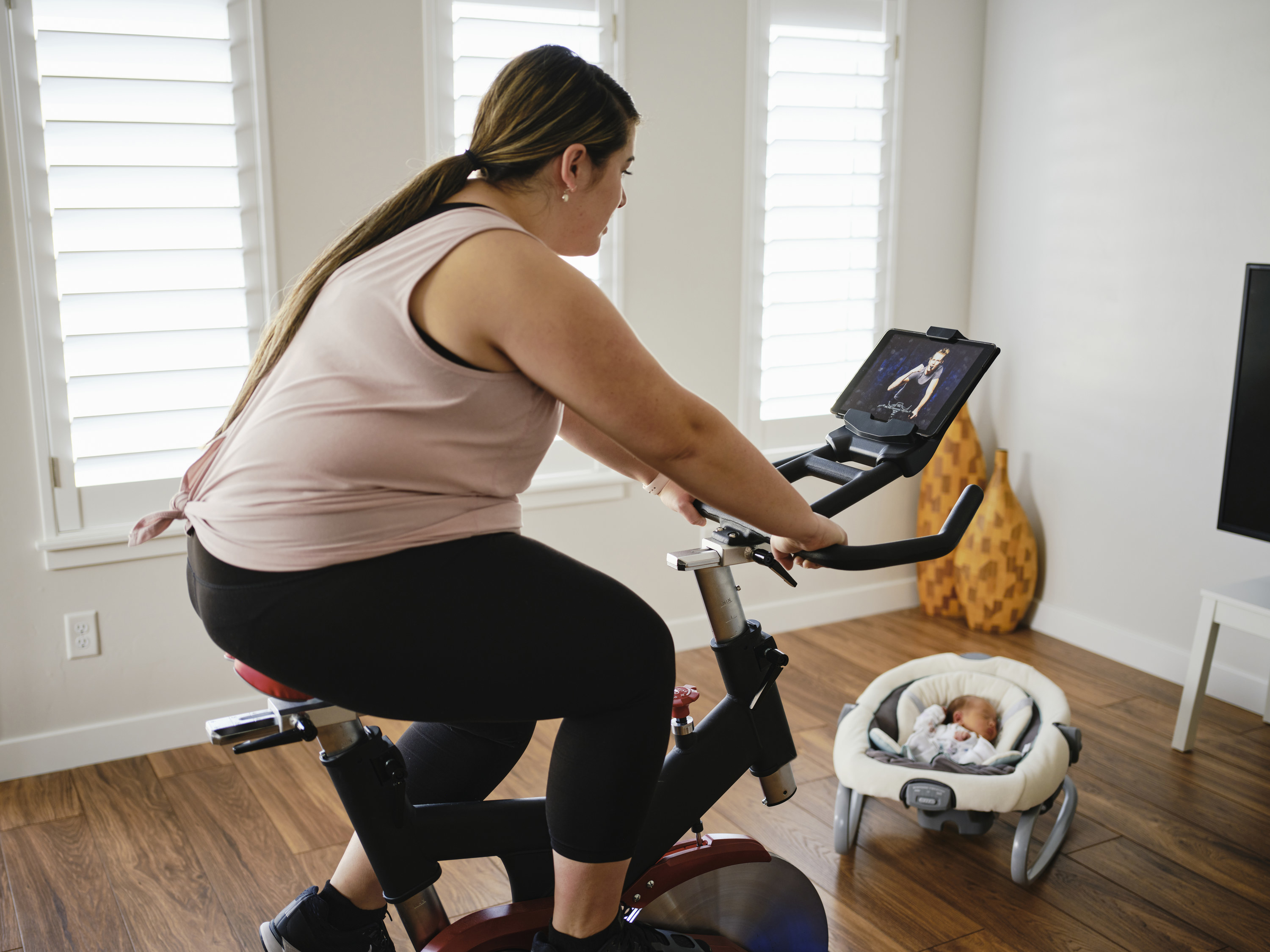 woman taking a peloton class at home with her baby nearby