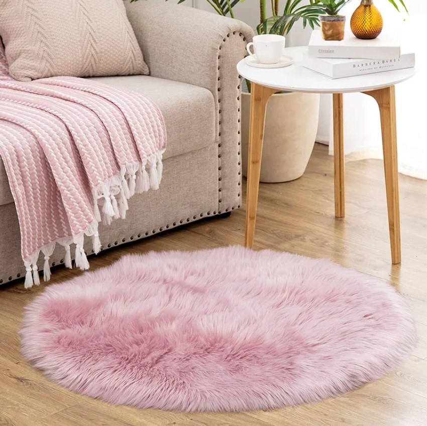 The round pink faux sheepskin rug on a hardwood living room floor