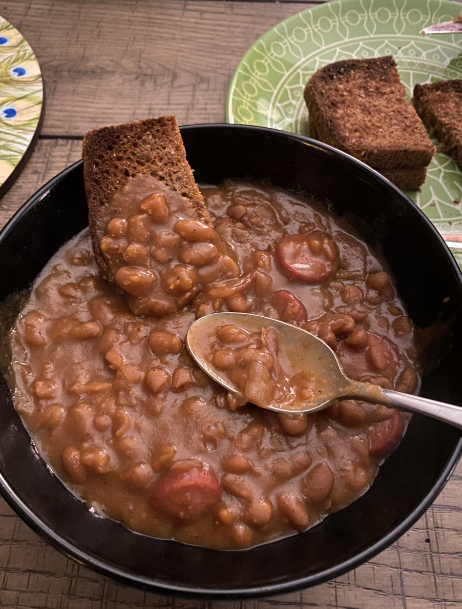 A skillet of baked beans with sliced hot dogs.