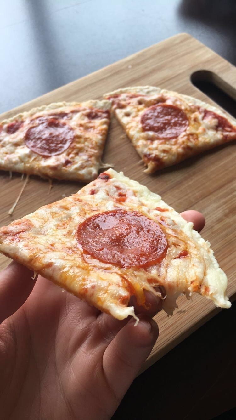 A hand holding pepperoni tortilla pizza.