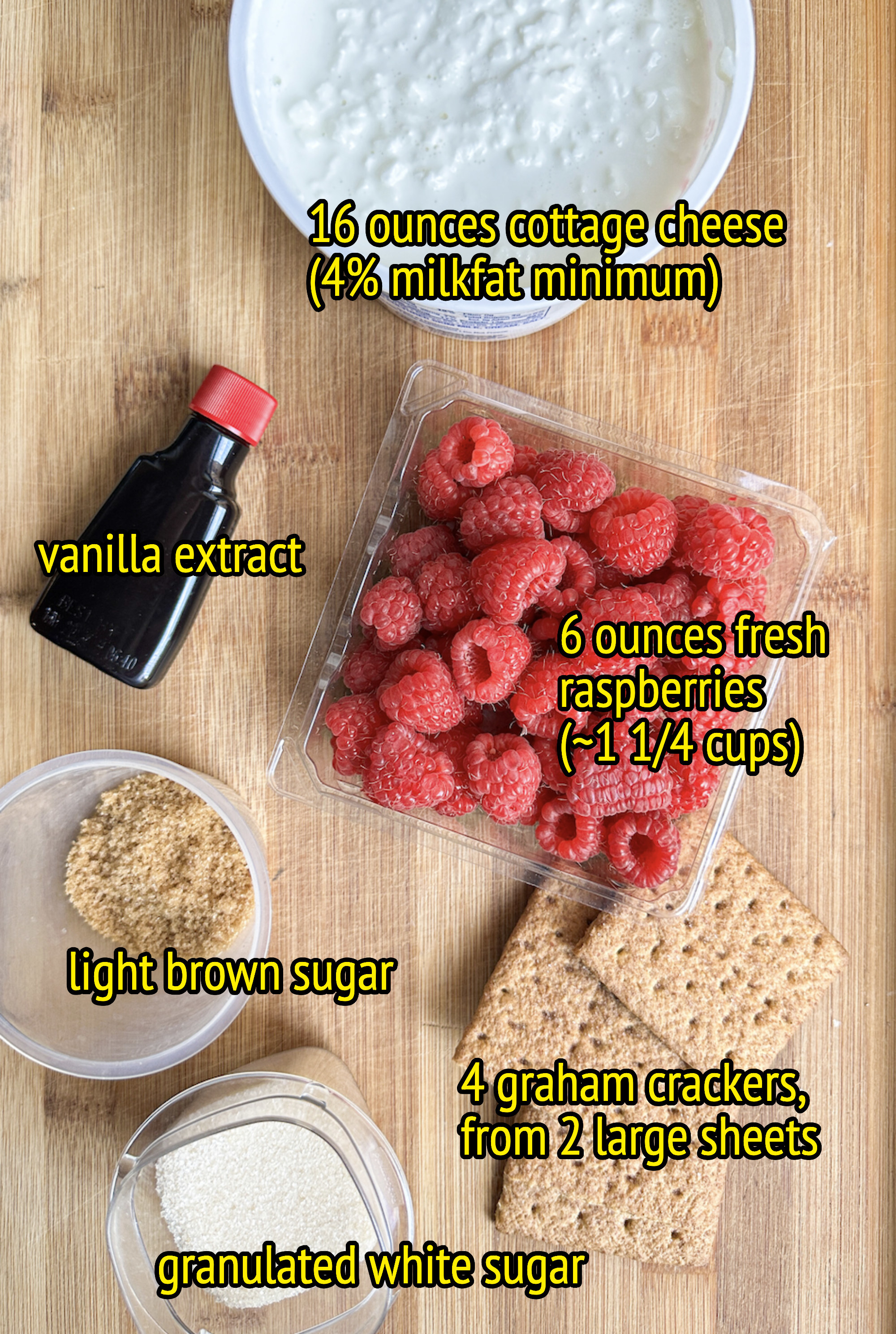 ingredients laid out on a cutting board: 16 ounces cottage cheese, 4% milkfat minimum, vanilla extract, 6 ounces fresh raspberries, light brown sugar, 4 graham cracker, granulated white sugar