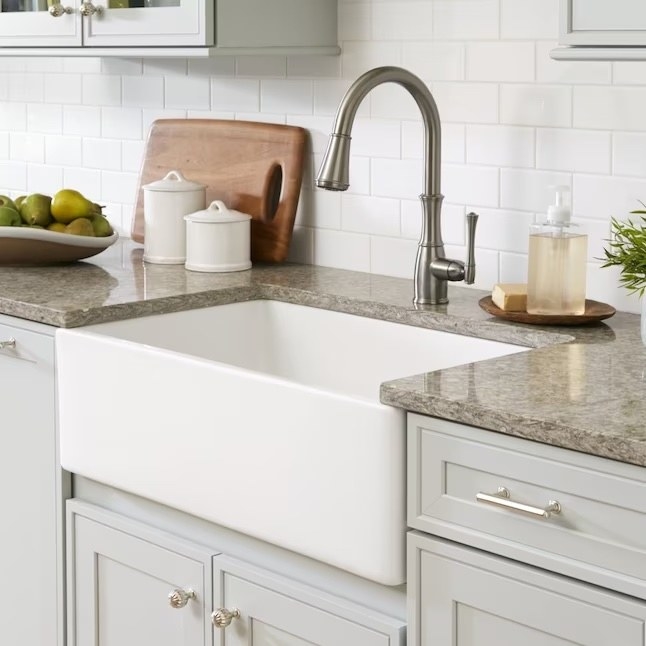 a white fireclay single bowl kitchen sink next to a granite countertop