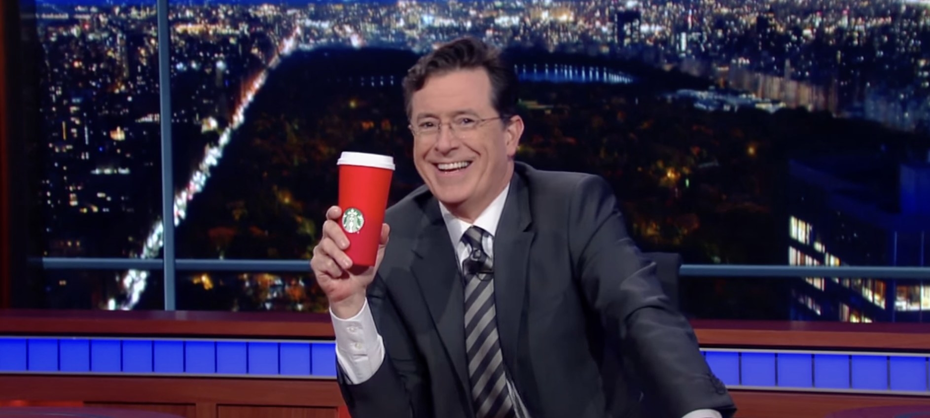 Stephen Colbert holds a red Starbucks cup