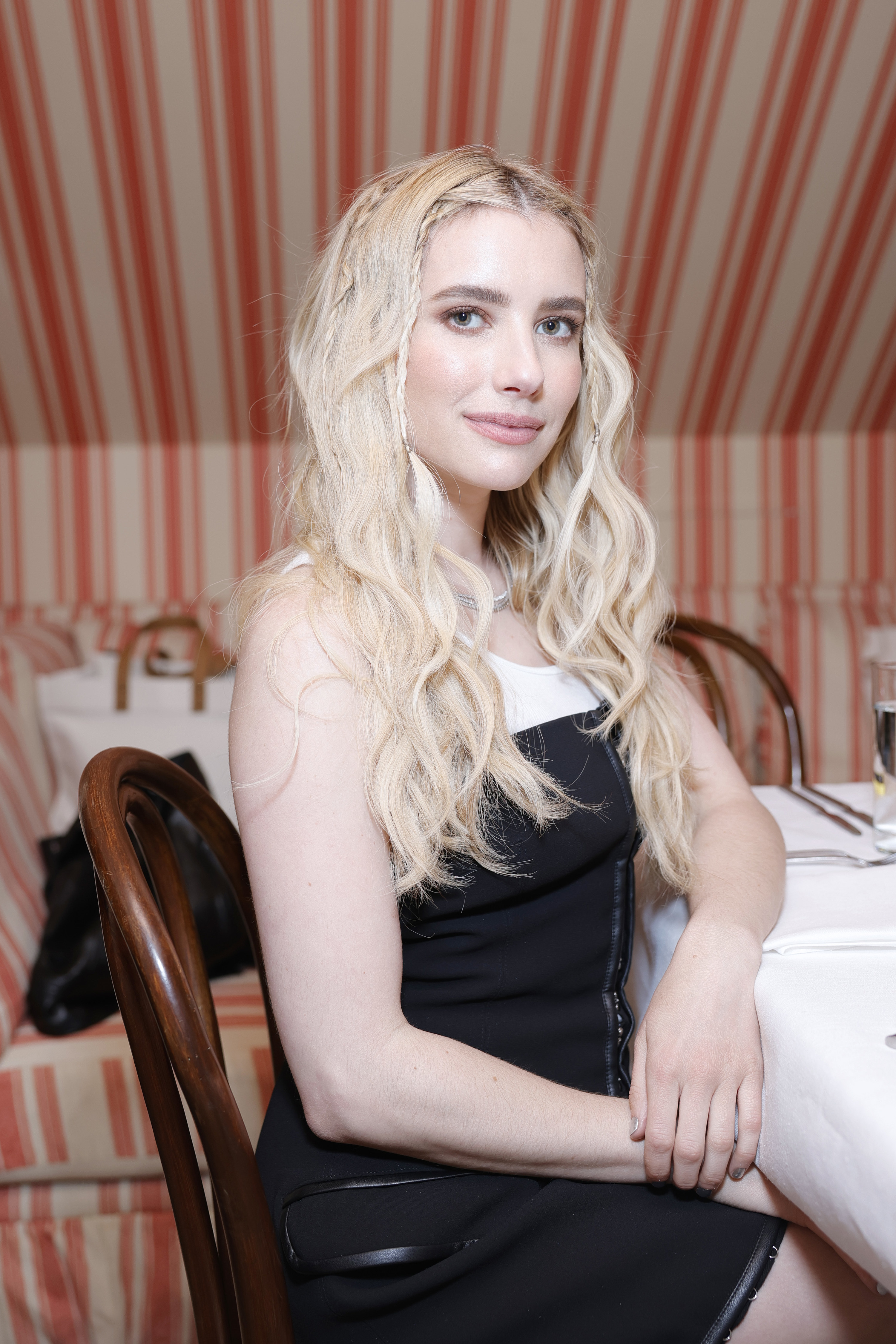 Emma Roberts seated at a table angled toward the camera and smiling slightly