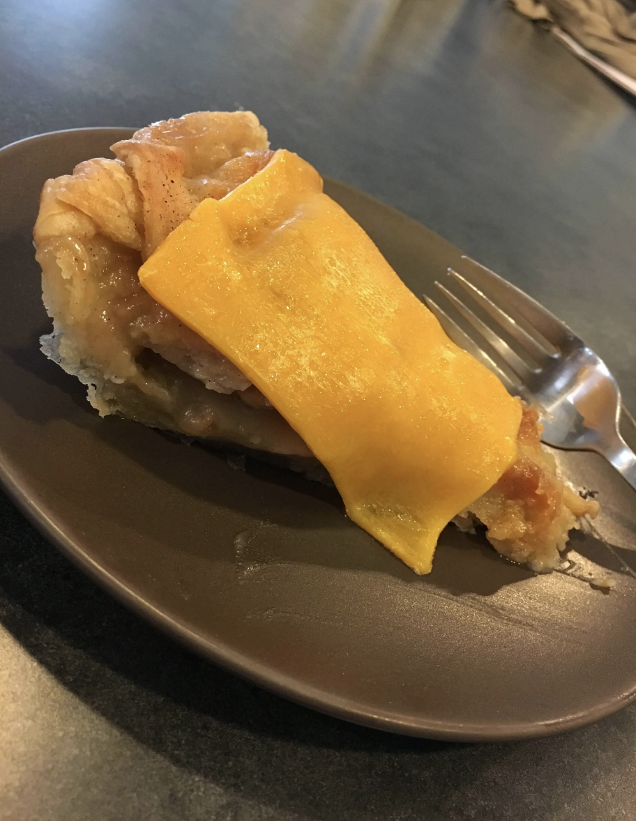 A slice of apple pie with melted Cheddar on top.