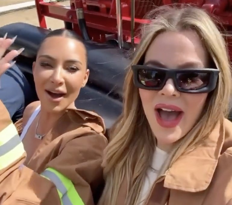 Khloe and Kim smile while riding in a firetruck