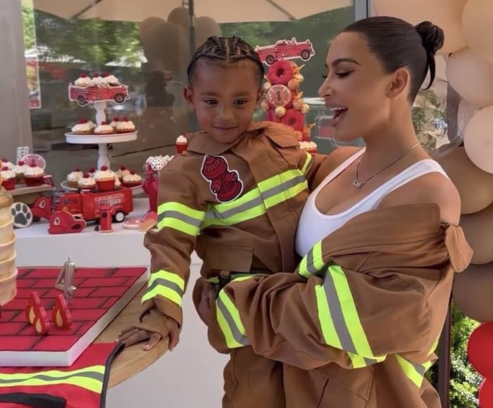 Kim holds Psalm in front of a table of cupcakes. They are both wearing fire fighters jackets
