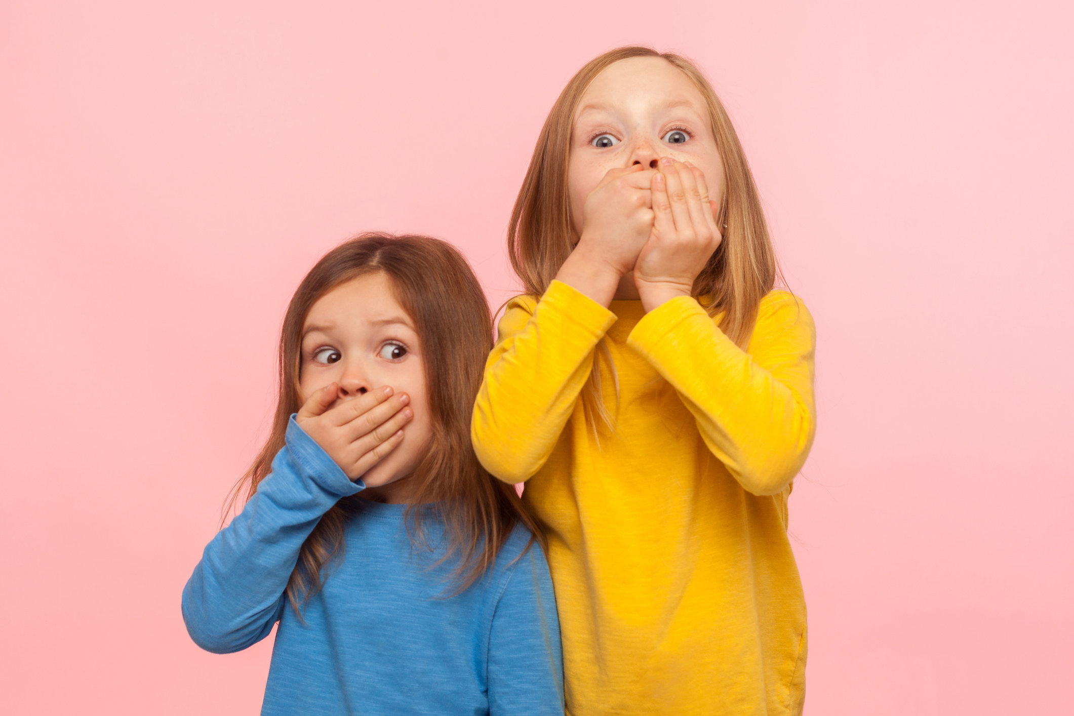 Two little girls covering their mouths