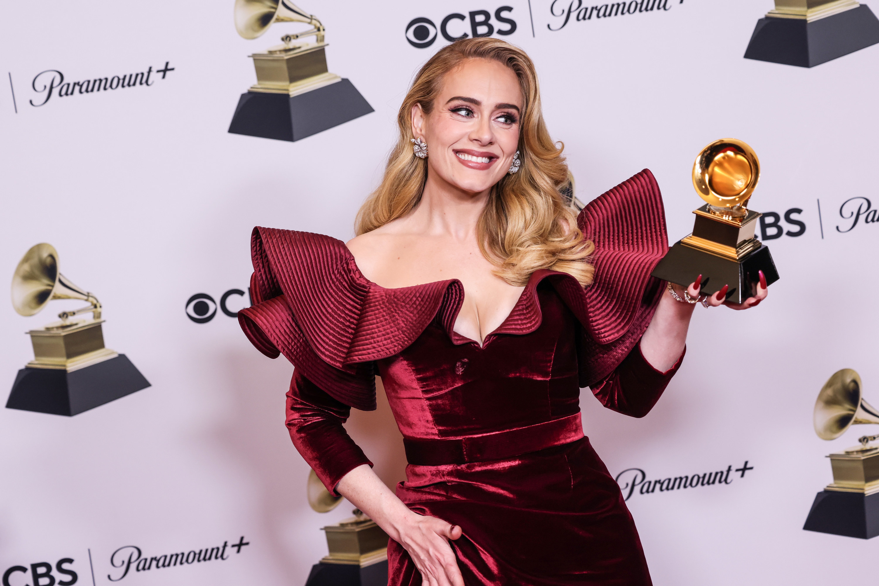 Adele holds up a Grammy trophy and smiles to the press after winning the award