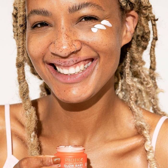 A person holding a small jar of eye cream with swatches on their eyes