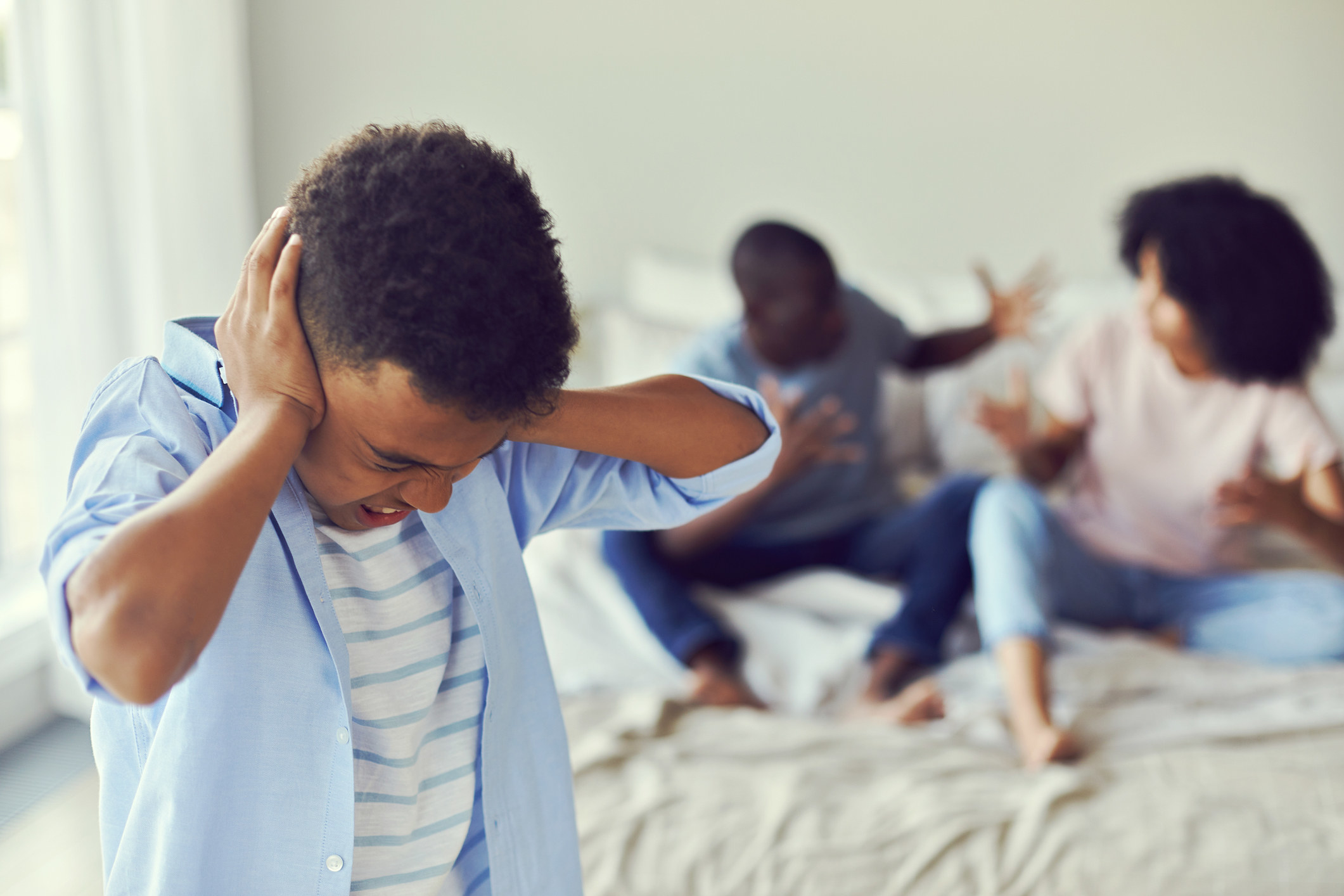 Kid holding hands over ears as his parents argue