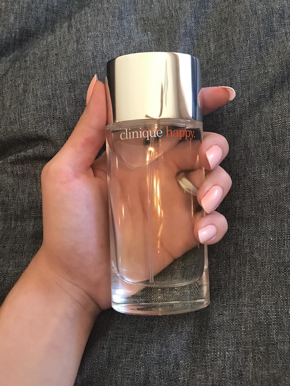 A reviewer holding the clear bottle of perfume with orange words