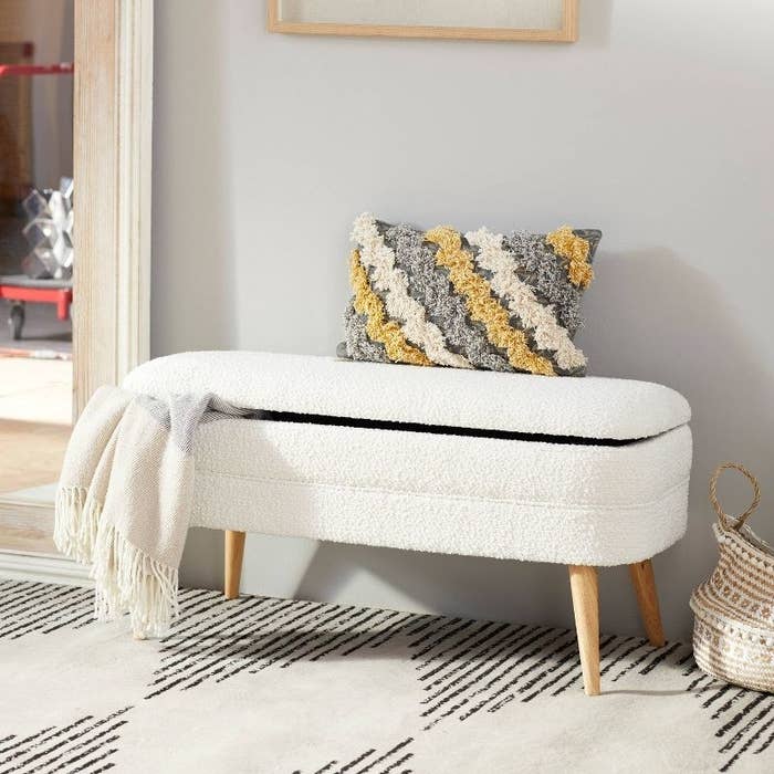 a white storage bench with wooden legs holding a blanket against a blue wall