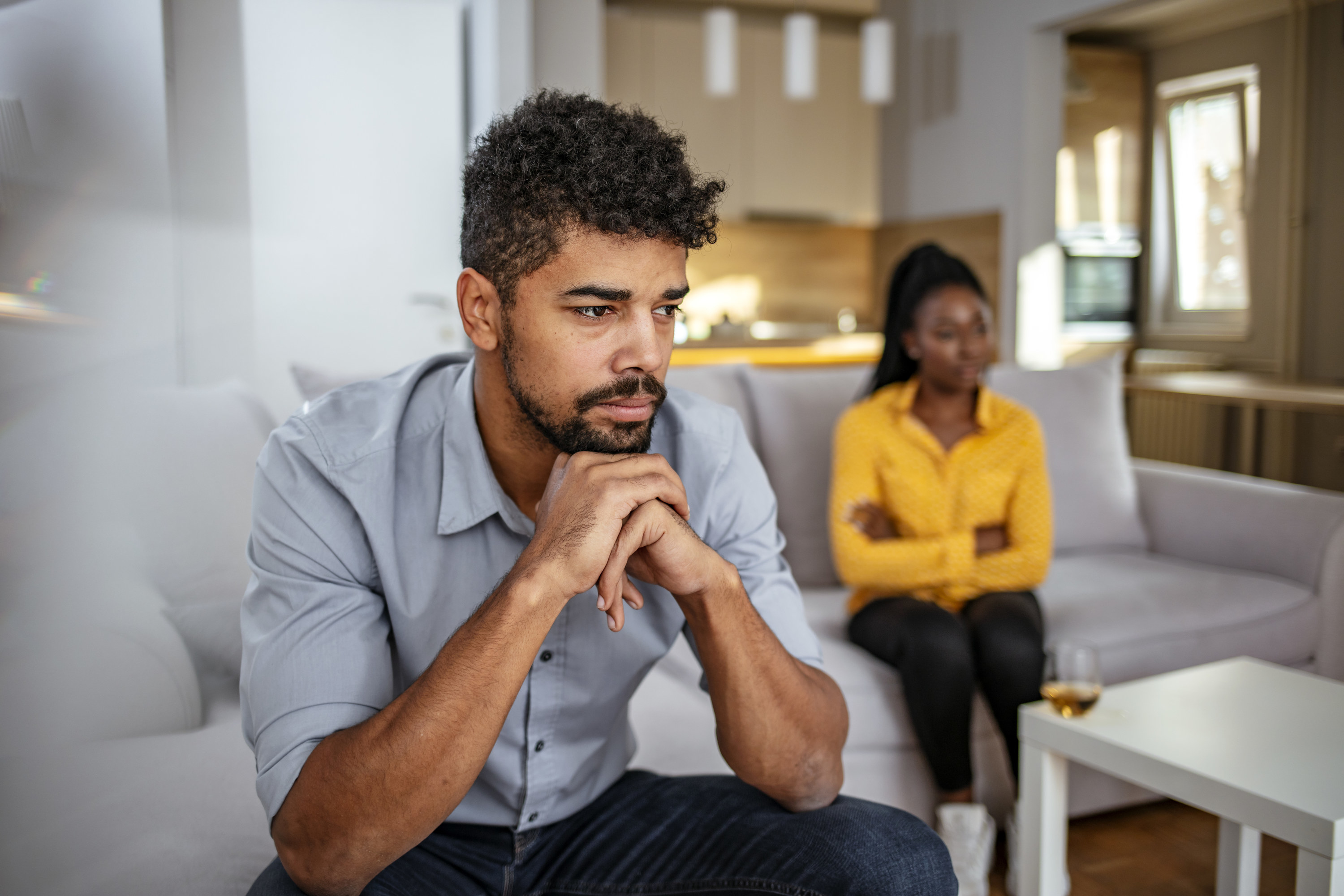 A couple sits at a distance from one another on their couch during an argument at home