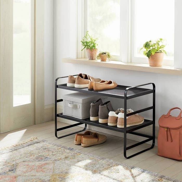 a two-tier black and metal shoe rack holding different shoes along a hallway