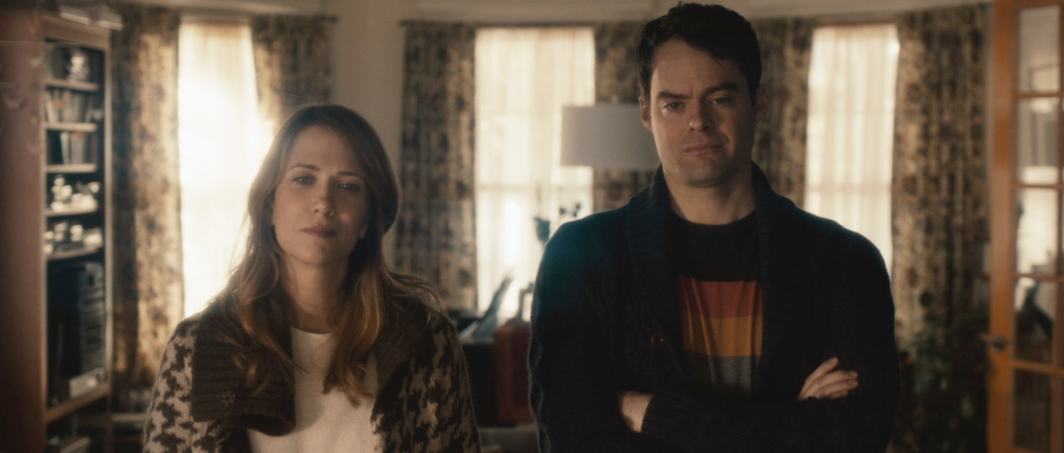 Kristen Wiig and Bill Hader stare at something off screen with their arms crossed