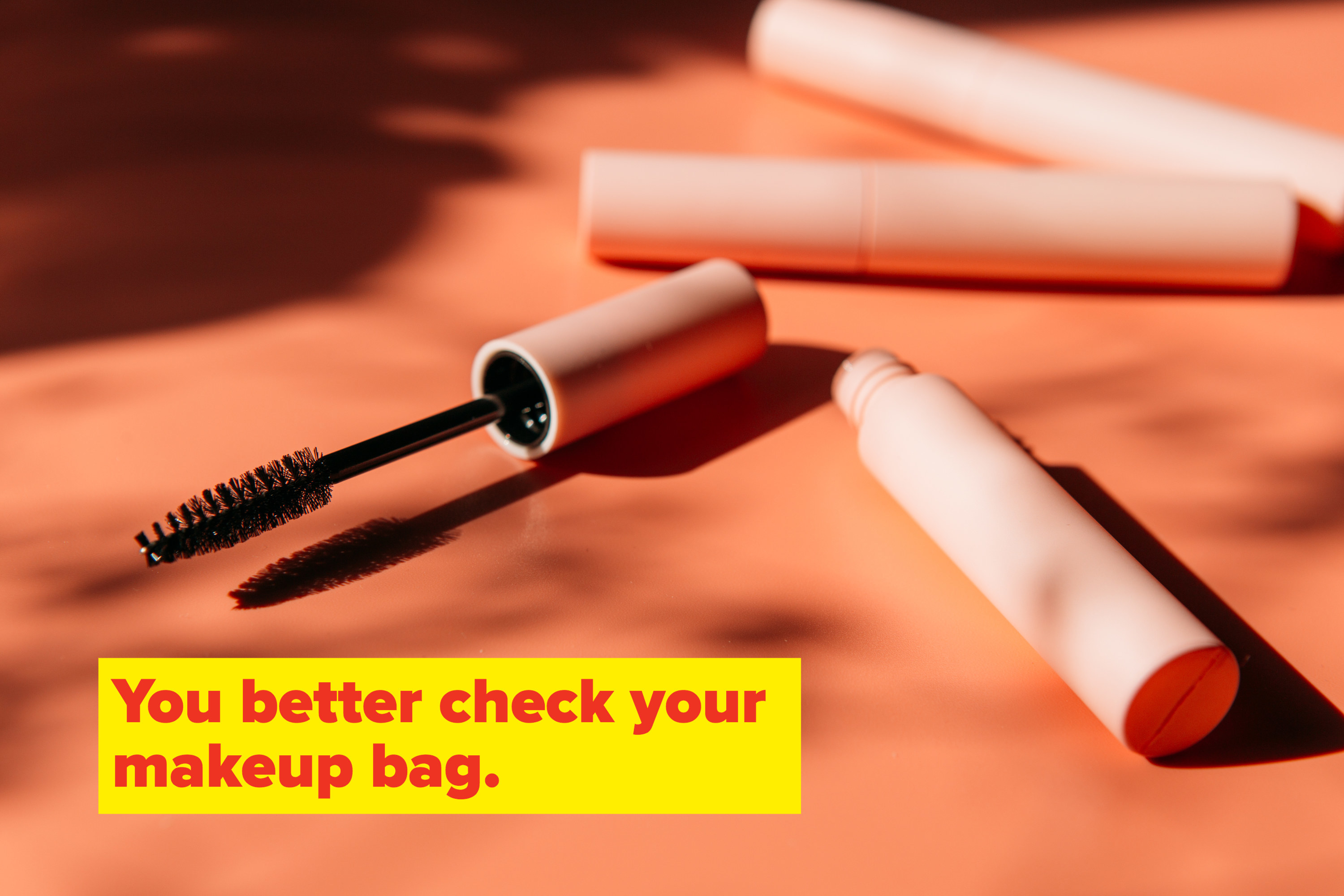 An opened tube of mascara laying on its side with two closed tubes in the background