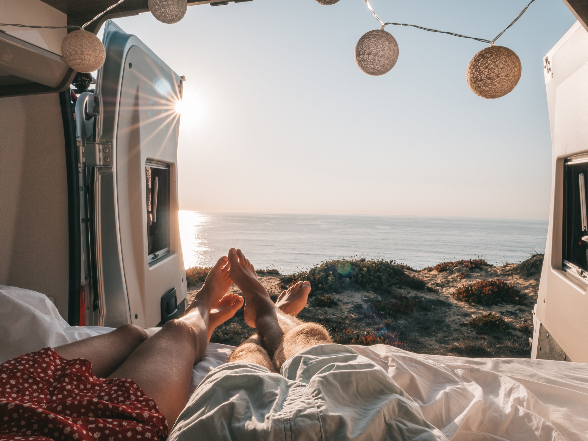 A couple sleeping in the back of a van by the ocean