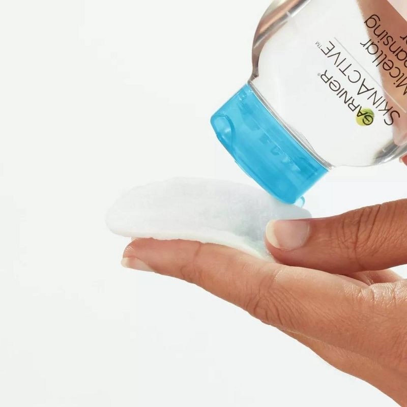 A person pouring micellar water on a cotton round