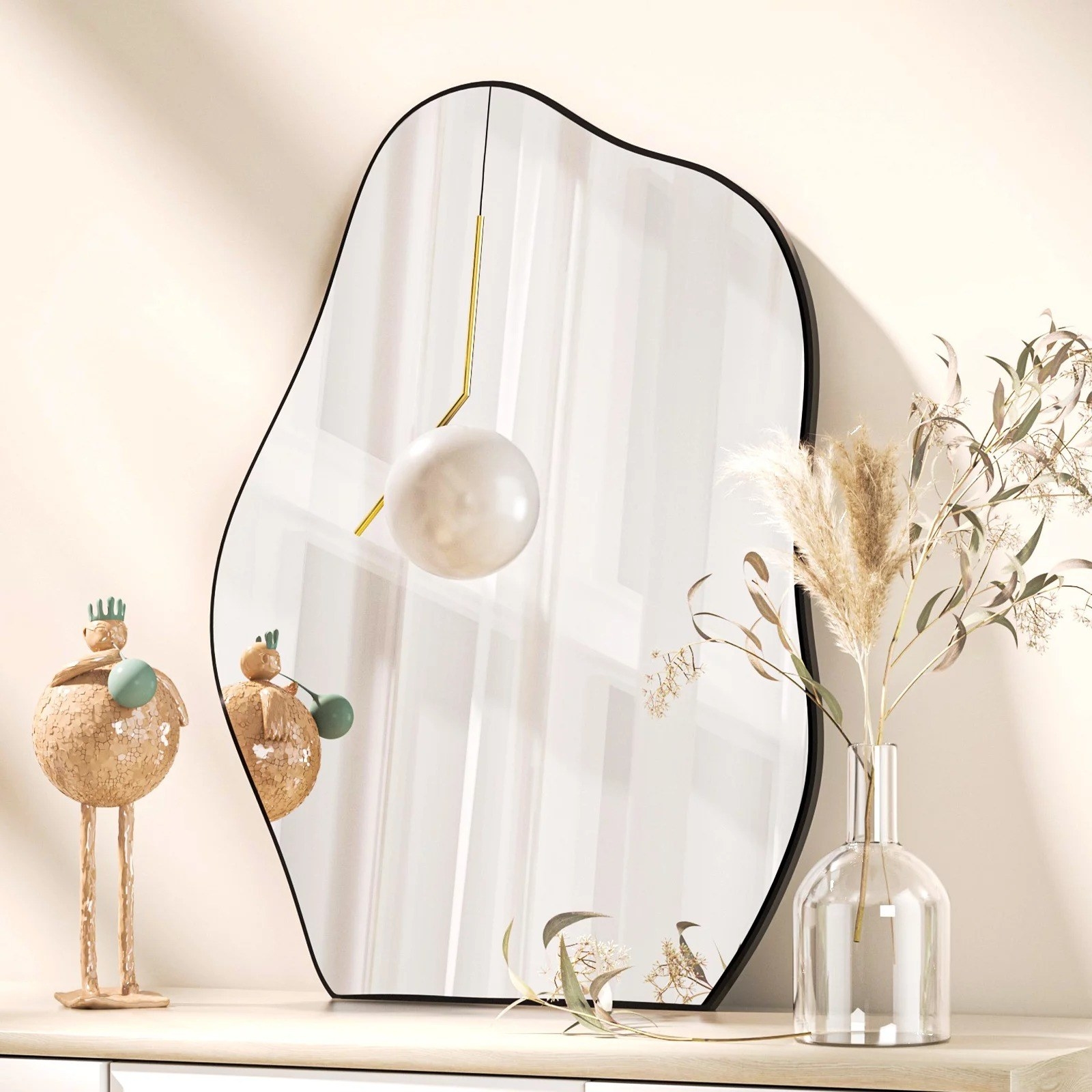 Wavy wall mirror on dresser top, next to decorative piece and clear vase with faux plants