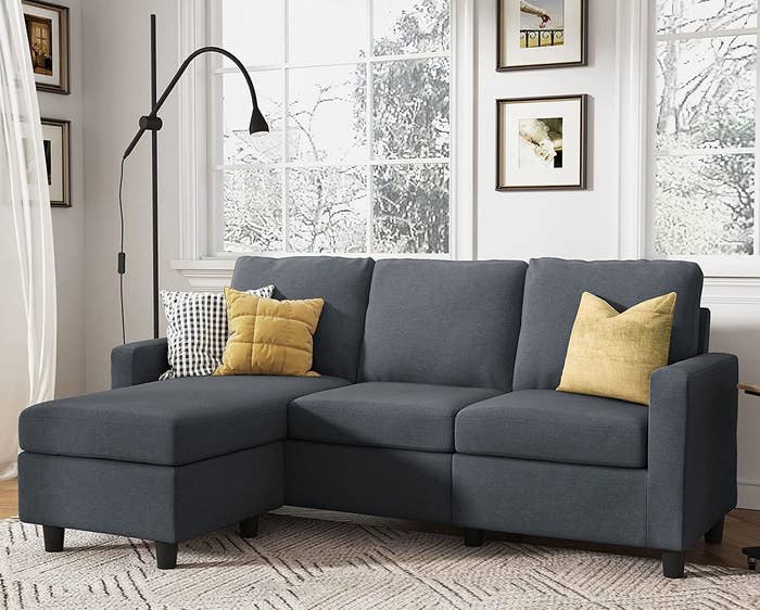 A dark grey sectional with yellow throw pillows is shown in a living room