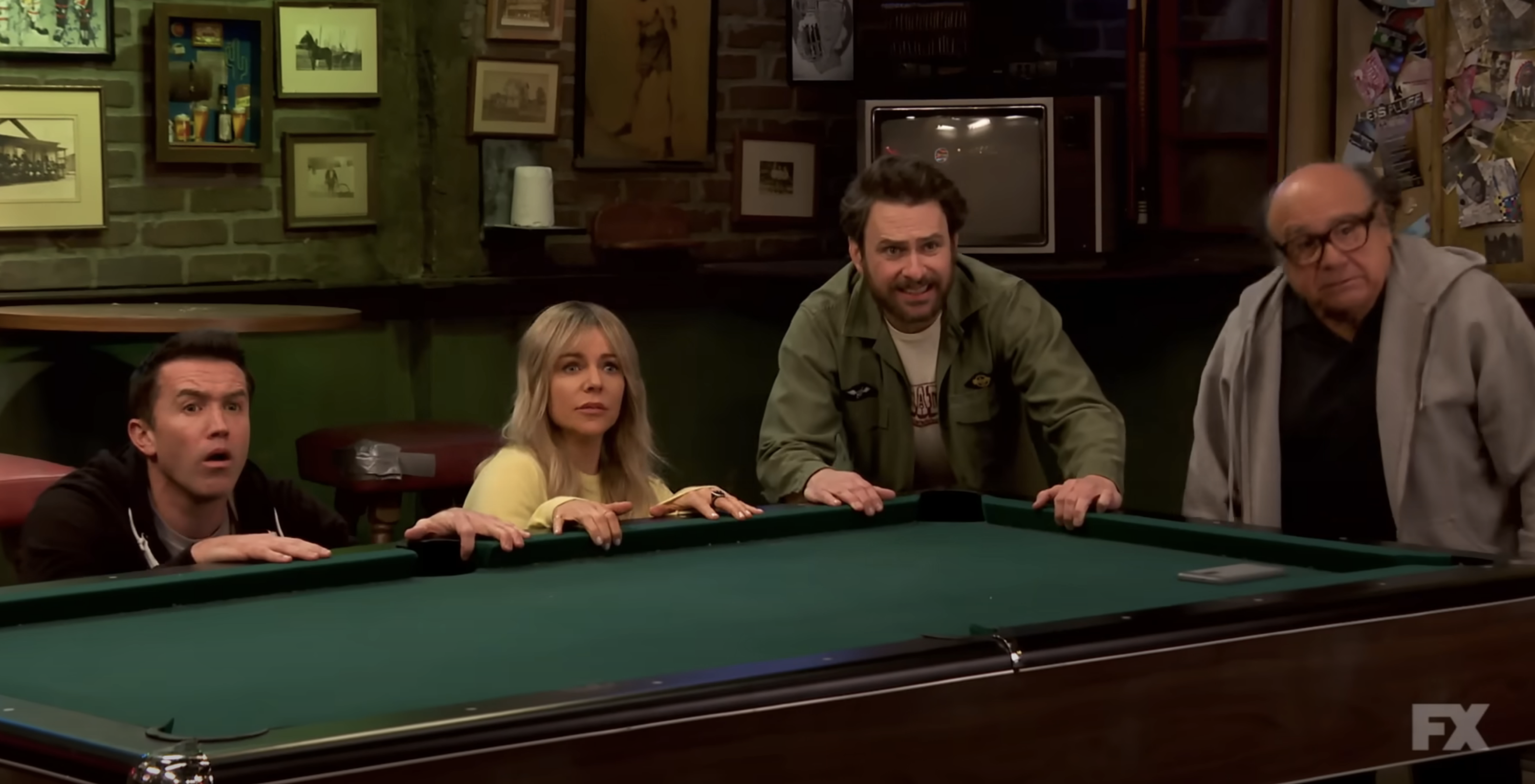 Four people standing or crouching around a pool table