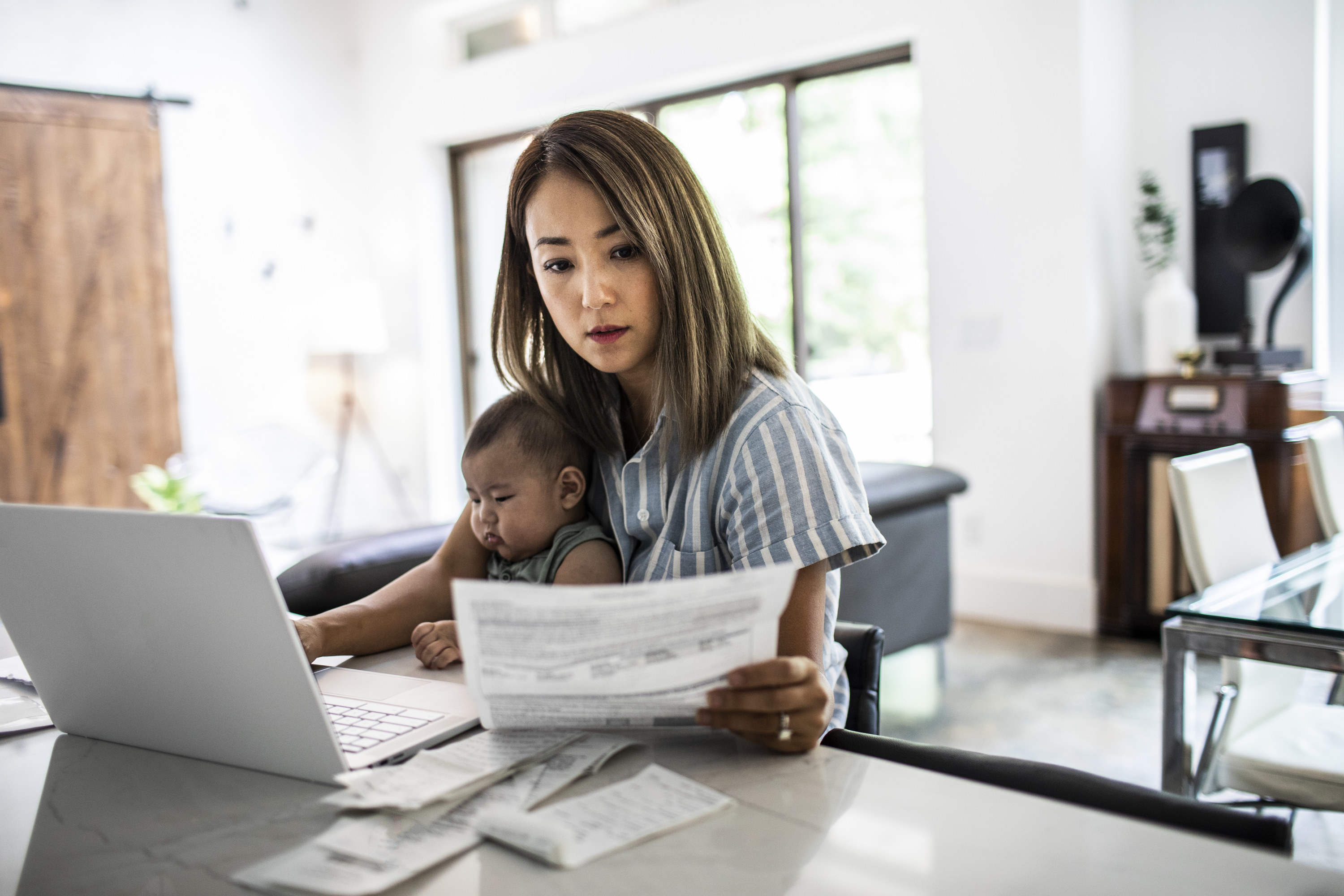 Woman holding a baby while working from home at a laptop