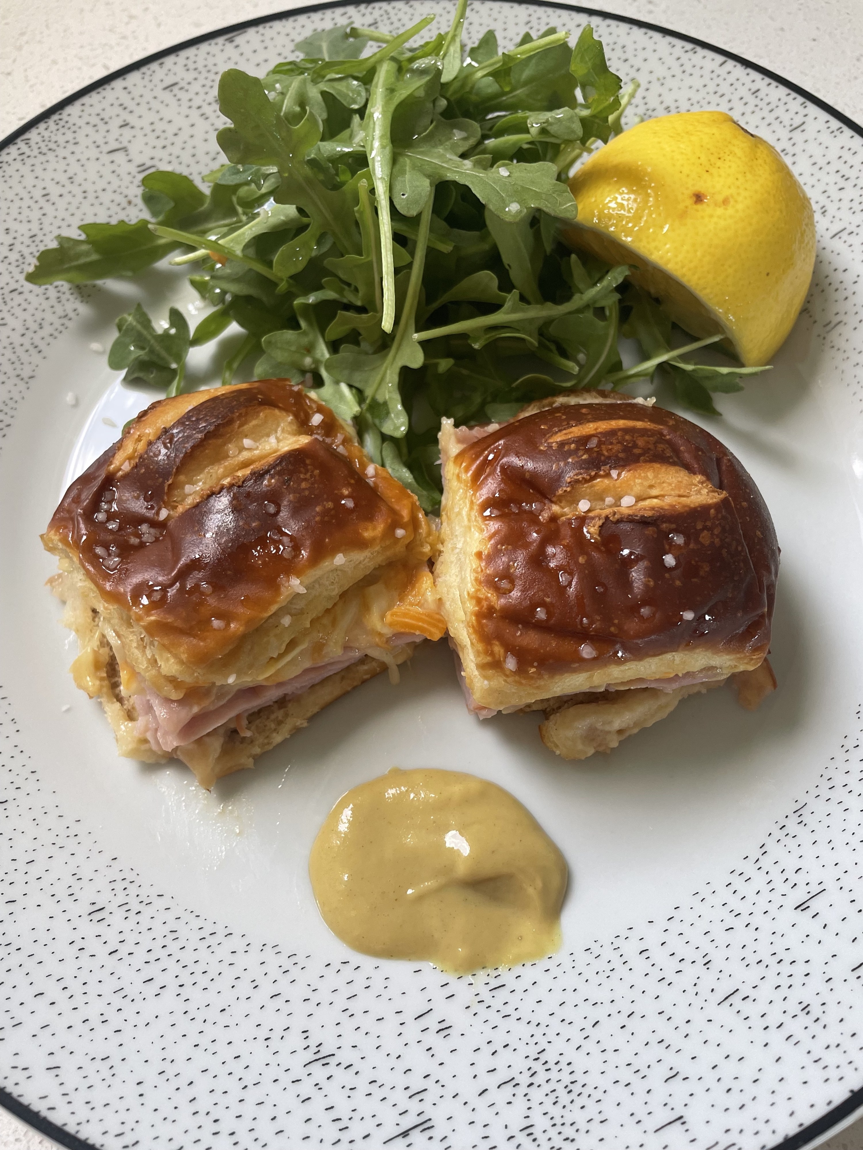 Ham and cheese sliders with dressed greens and honey mustard on a plate