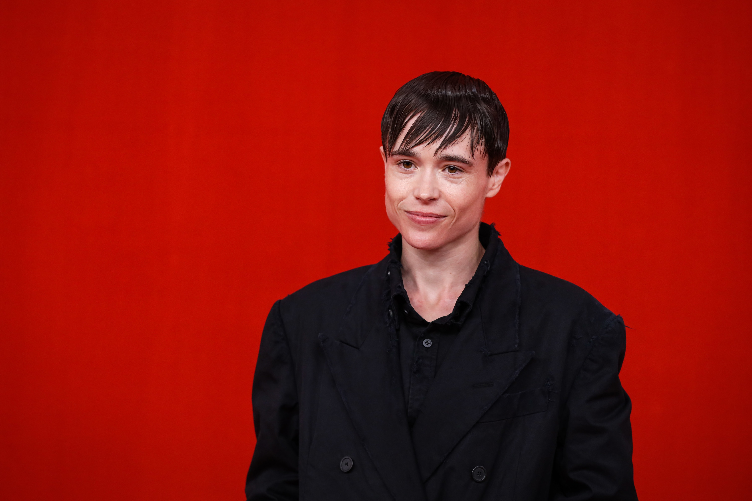 Close-up of Elliot in a suit jacket and shirt against a plain red background