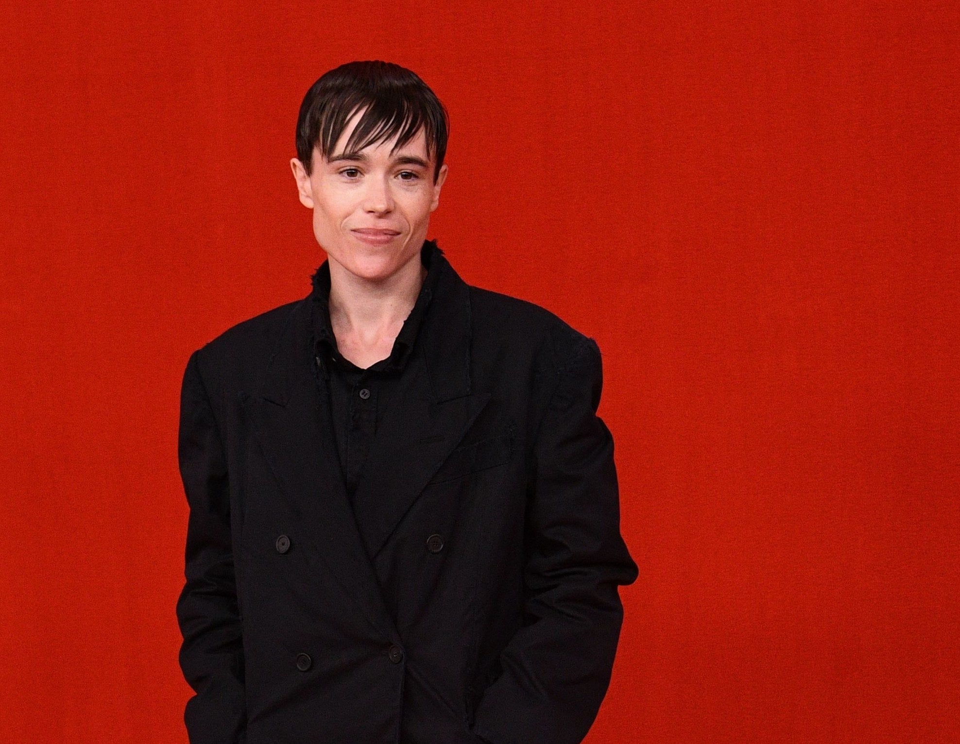 Close-up of Elliot in a suit jacket and shirt against a plain red background