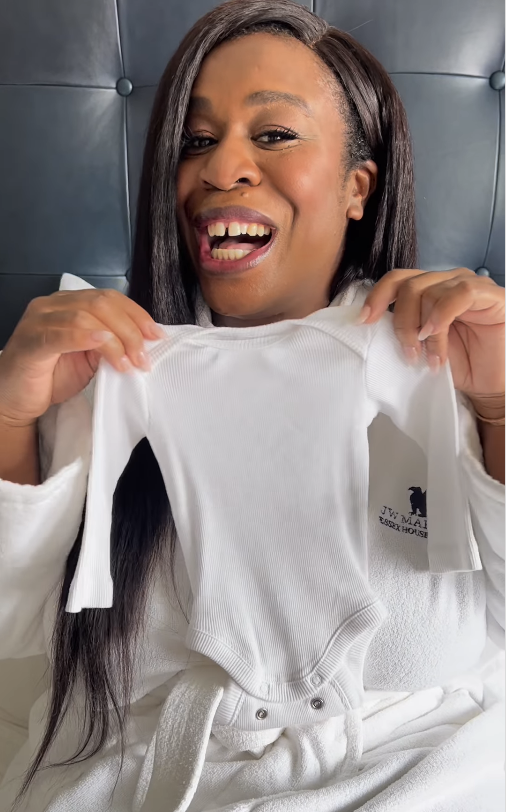 Uzo Aduba holding up a baby onesie and smiling