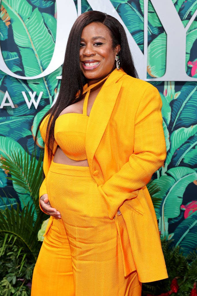 Uzo cradling her baby bump as she rocks an open suit and bra-style top and high-waisted pants