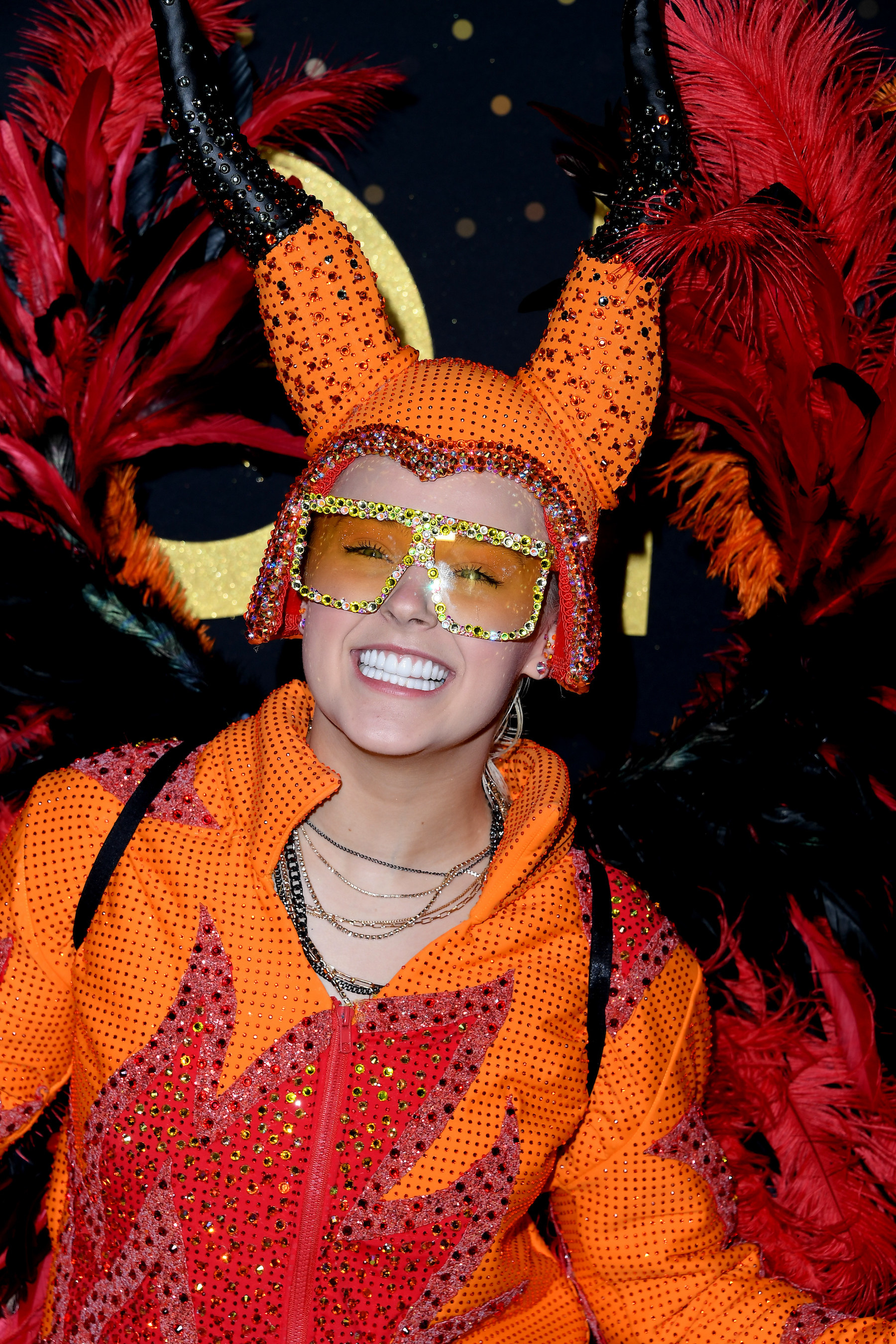 JoJo smiles widely as she rocks a bedazzled jacket with flame details and large bedazzled tinted glasses