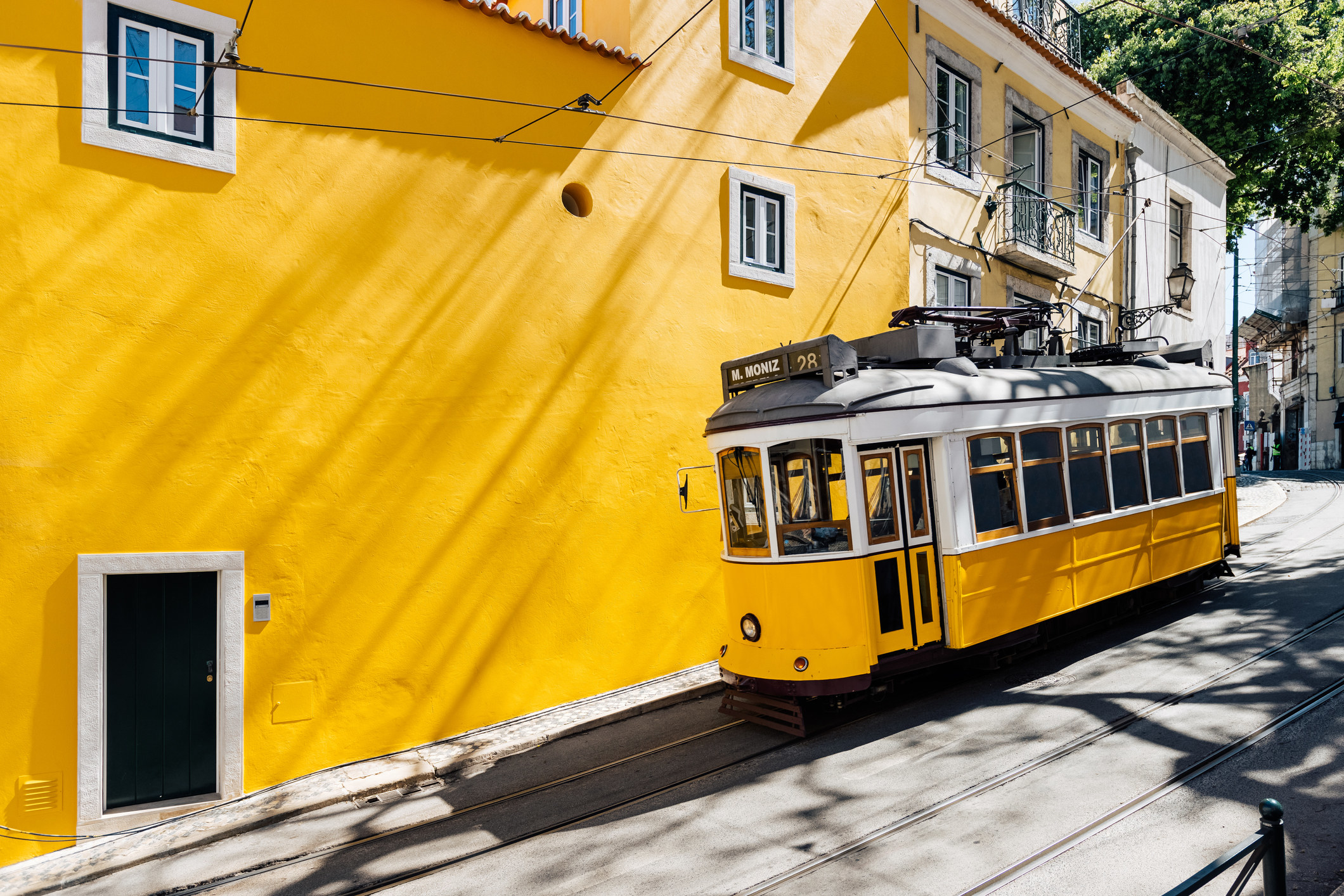 A yellow tram moving past yellow building in Lisbon