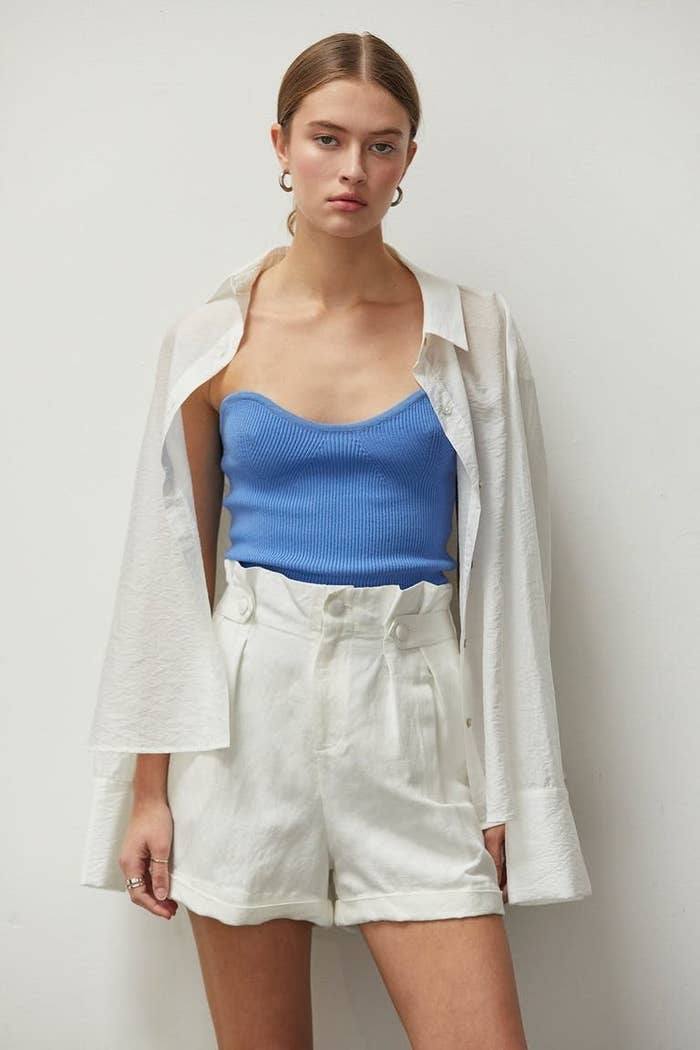 Model wearing pleated linen shorts in white with blue shirt and white linen over shirt
