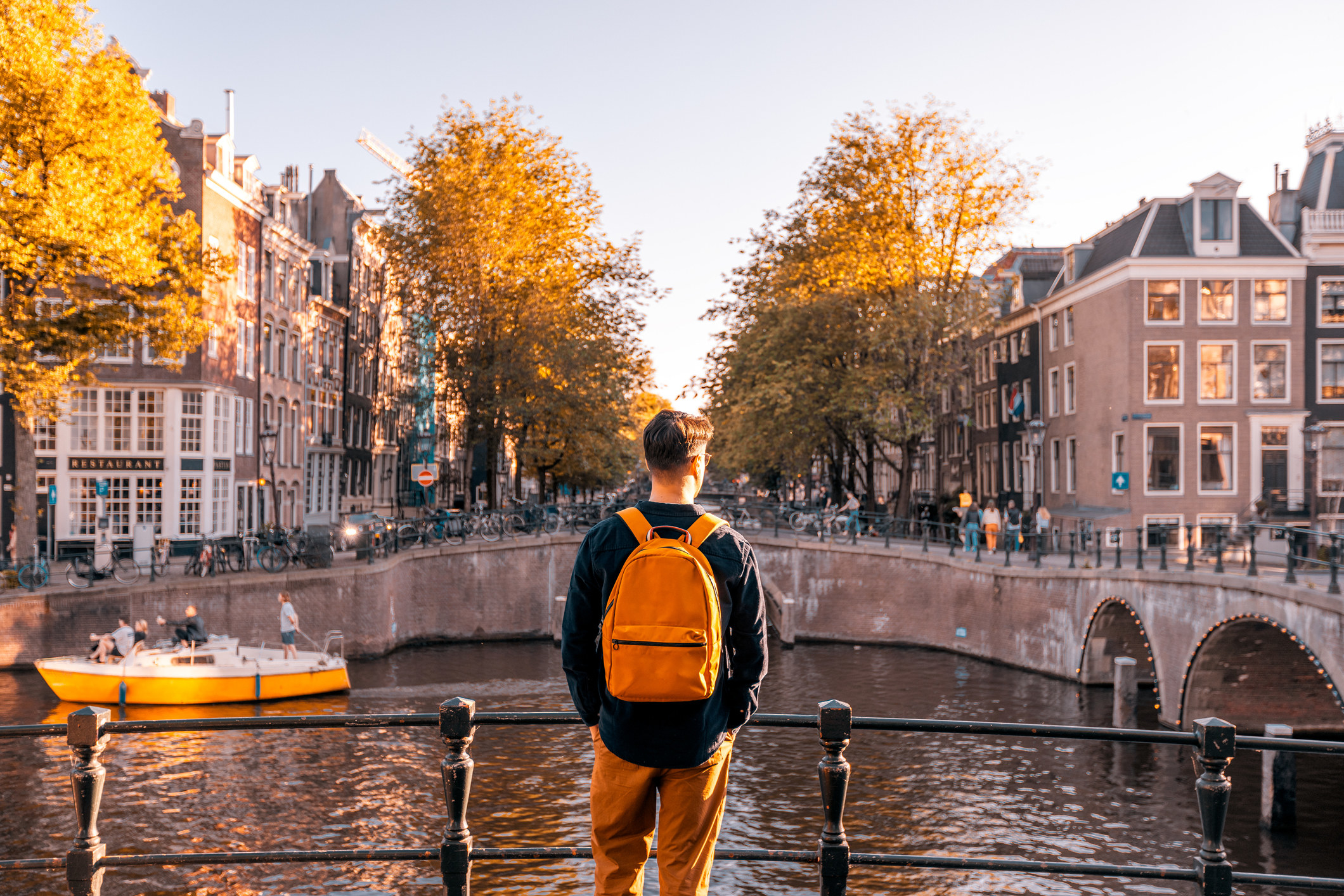 Rear view of a man wearing a backpack and looking at an Amsterdam canal on a sunny day