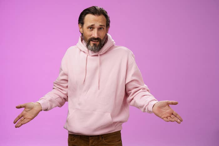 Closeup of a man in a light-pink hoodie shrugging with his arms out