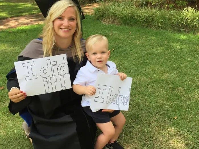The author at her graduation with her son; she&#x27;s holding up an &quot;I did it!&quot; sign and he&#x27;s holding an &quot;I helped&quot; sign