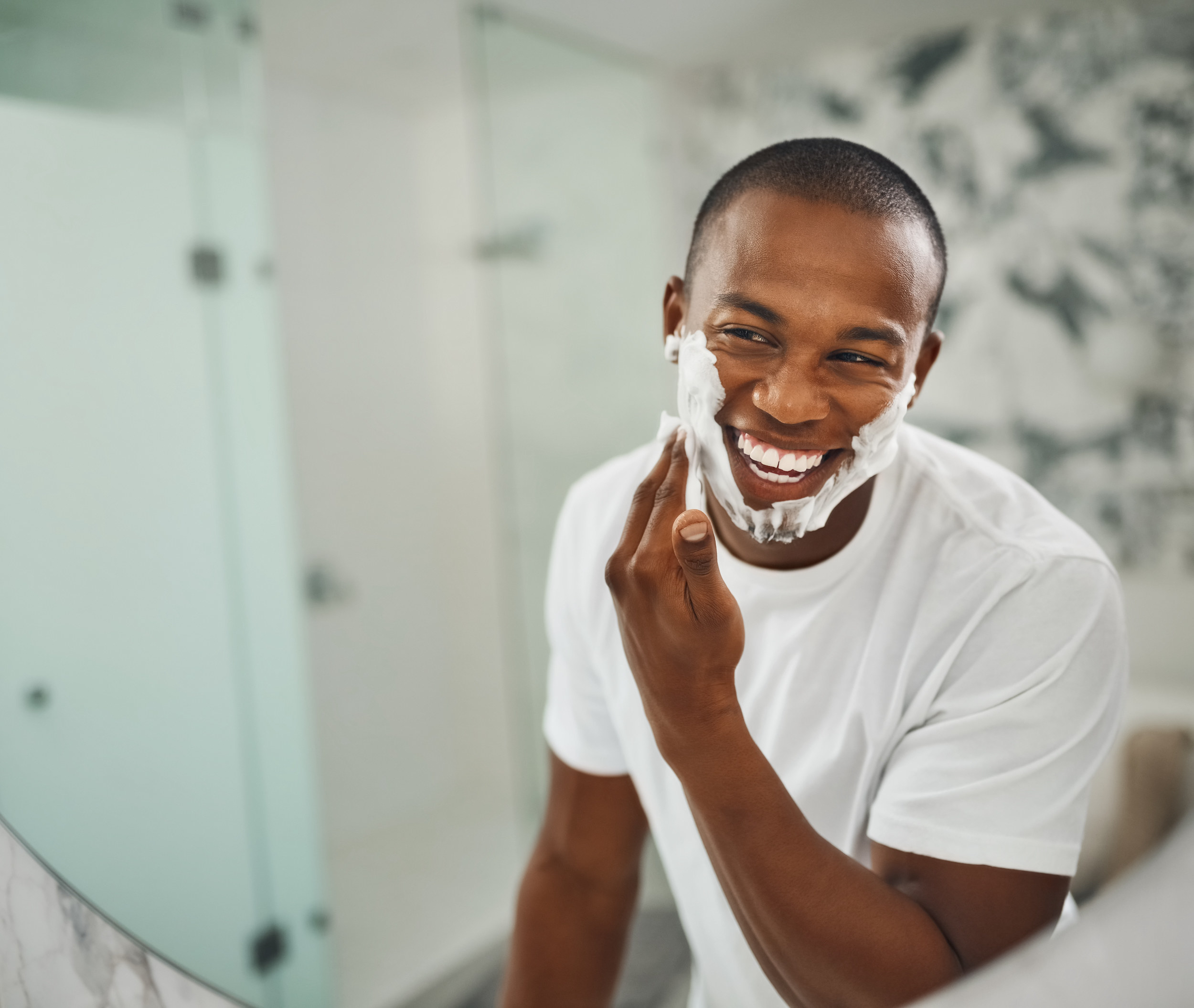 A man applying shaving cream to his face and smiling
