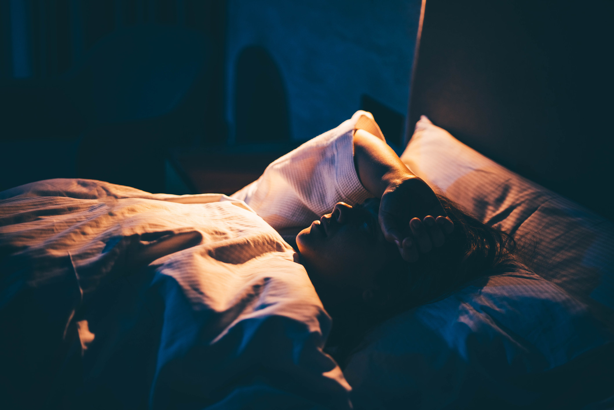 A woman in bed with her arm draped over her forehead