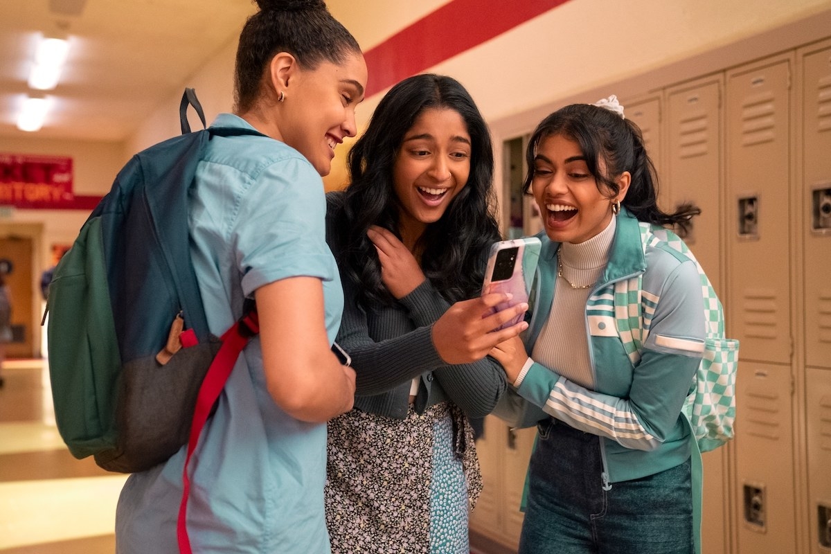 A scene from NHIE with Devi and friends looking at a cellphone in the school hallway in front of the lockers
